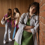 Dans l'image nous pouvons apercevoir deux jeunes filles en arrière-plan se moquant et délaissant la jeune fille qui se tient contre le mur devant elle, nous pouvons observer de la tristesse sur son visage